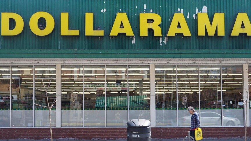 A scruffy man with a plastic bag walks past a bargain shop