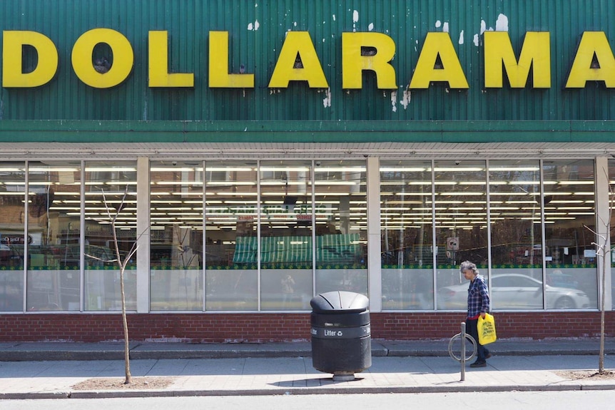 A scruffy man with a plastic bag walks past a bargain shop