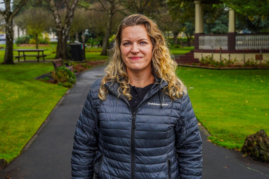 A woman in a black puffer jacket smiles for a photo in a park.