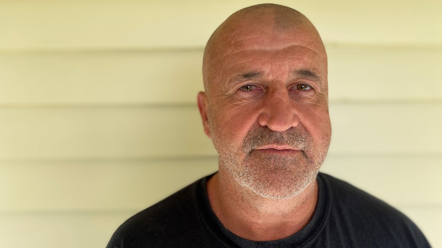 Rod Owen stands in front of a cream coloured wall and looks at the camera.