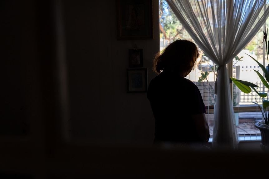 A silhouette of a woman standing in front of a window in a dimly lit room.