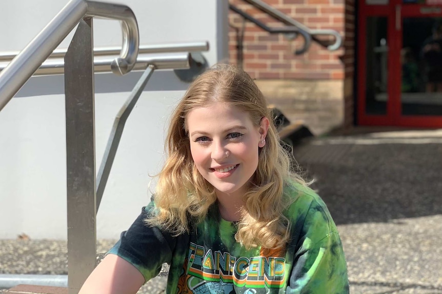 A young woman with long blonde hair sits on stairs.