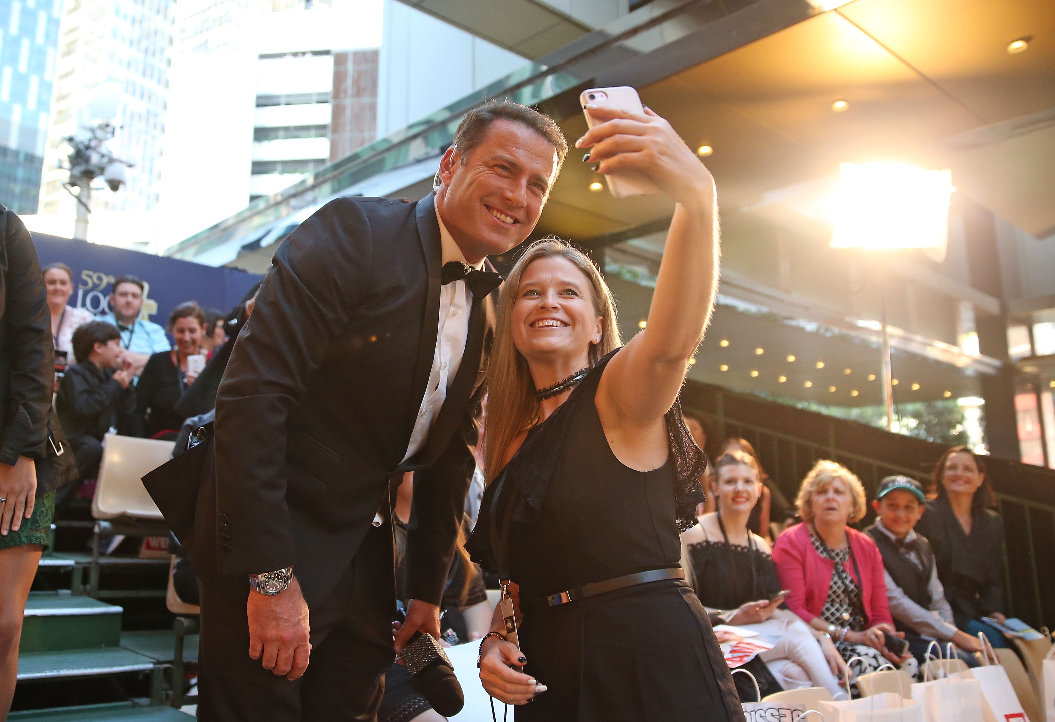 Karl Stefanovic posing for a selfie with a female fan who is holding an iPhone, a crowd beh