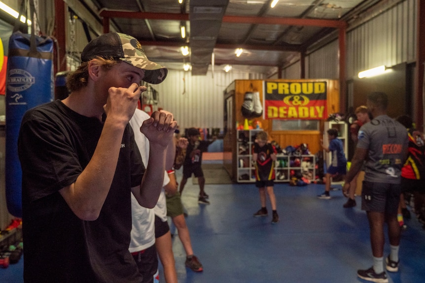 A young men stand and practise their boxing skills, watched by an older instructor 