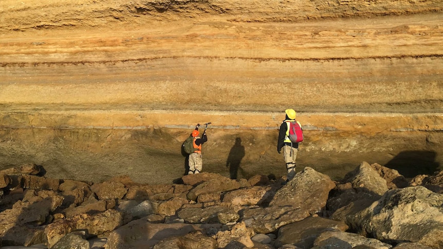 Two researchers at base of cliff