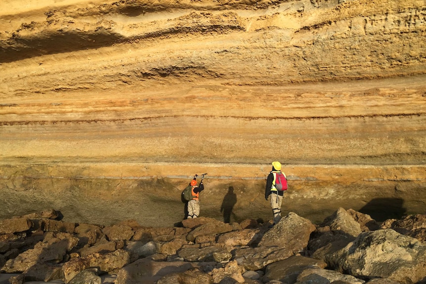 Two researchers at base of cliff
