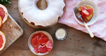 An overhead shot of a bundt cake surrounded by a plate of sliced grapefruit and coffee.