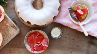 An overhead shot of a bundt cake surrounded by a plate of sliced grapefruit and coffee.