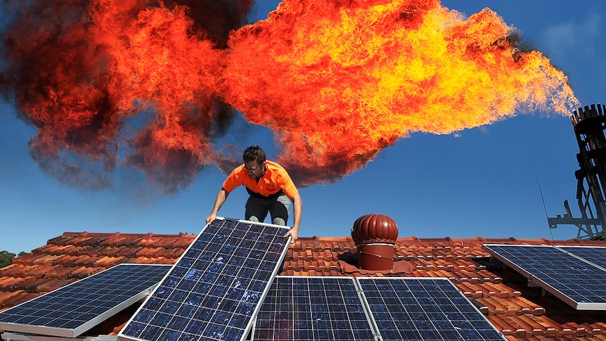 A worker installing rooftop solar panels with a industrial chimney venting a big flame behind.