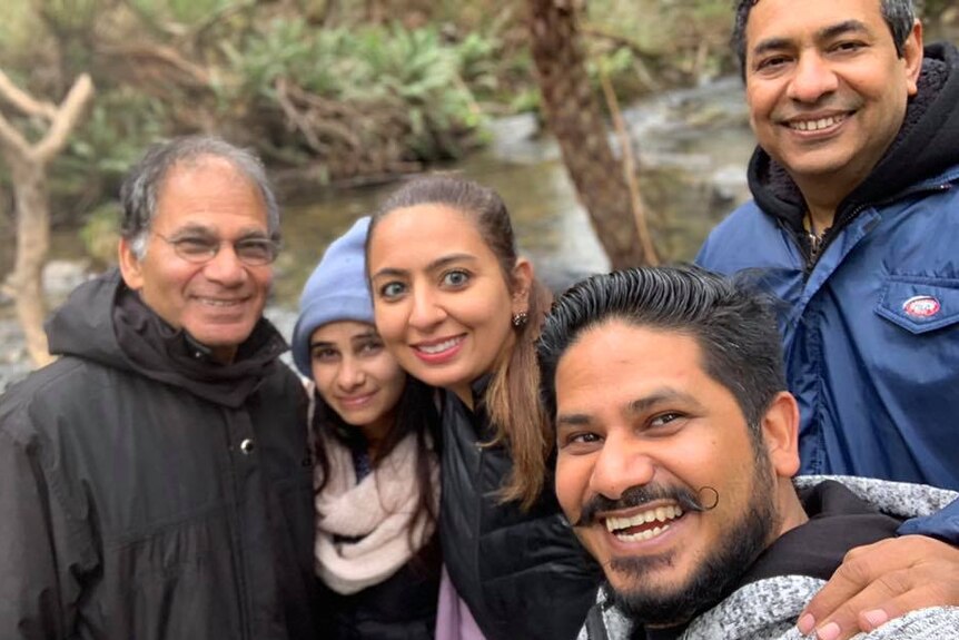 The Gupta family — two women and three men — poses for a photo together. They are smiling by a riverbank.
