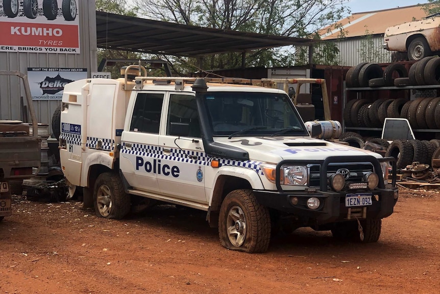 A police vehicle in front of an auto shop with its tyres slashed.