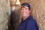 Farmer laughing in front of stacks of hay bales.