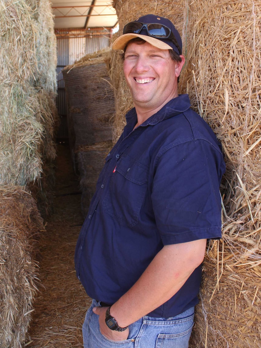 Farmer laughing in front of stacks of hay bales.