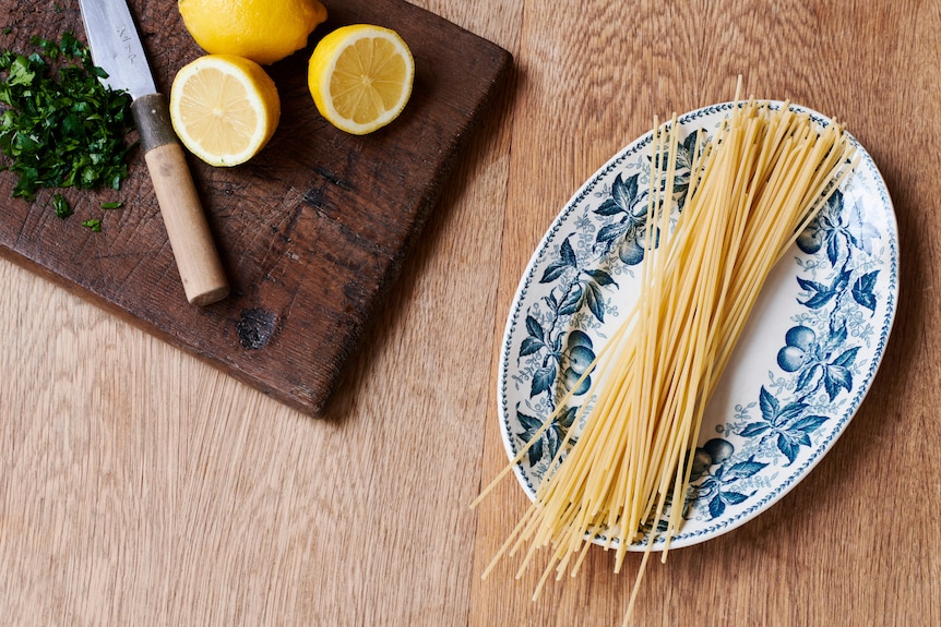 Dried spaghetti on a plate, lemons and parsley on a chopping board. Ingredients for spaghetti with prawns, parsley and garlic.