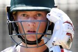 A woman wearing a cricket helmet, gloves and shirt stares intently into camera
