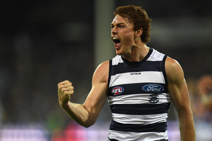 Gary Rohan pumps his fist and screams with his mouth wide open in a blue and white striped singlet