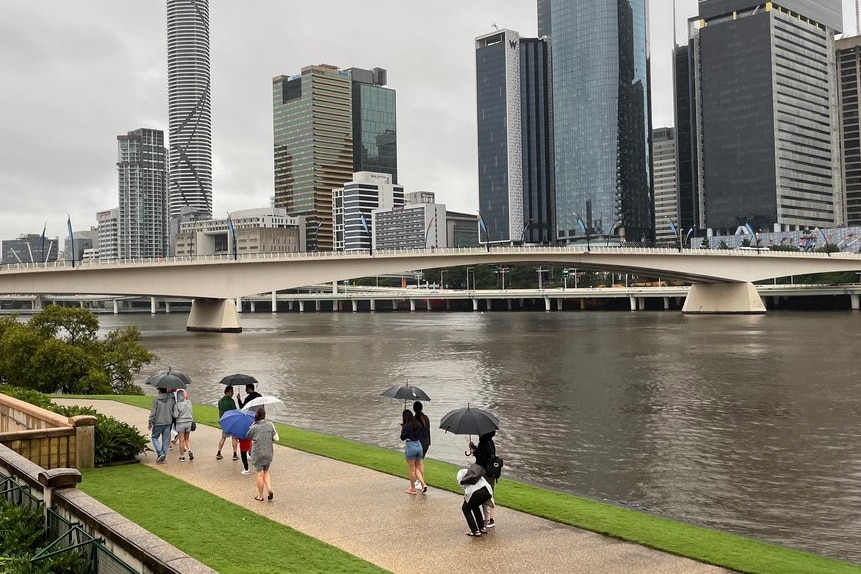 People carrying umbrellas walk by the Brisbane River in the rain on April 4, 2021.