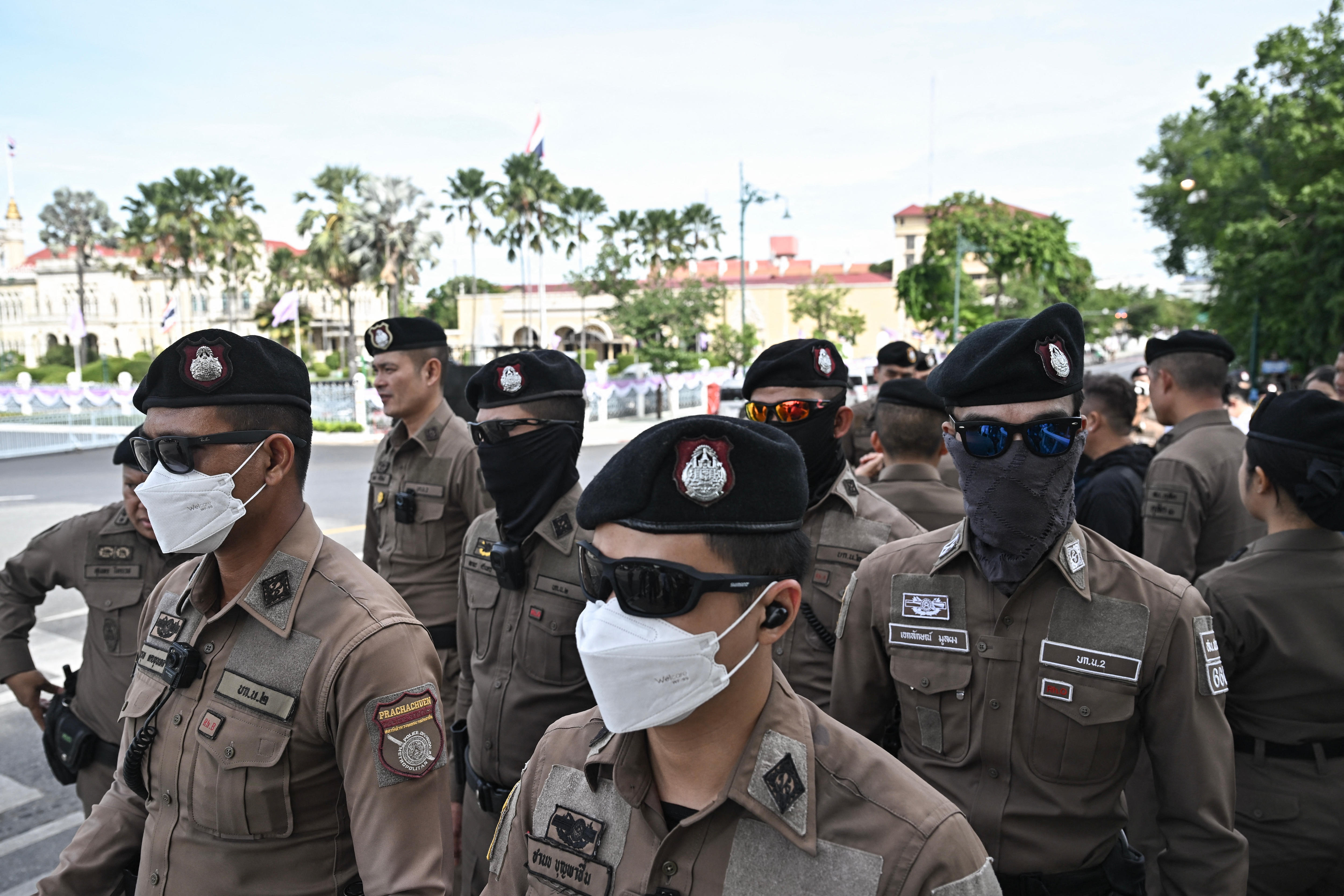 Thai police officers, many in masks, walk outside a government building in Bangkok