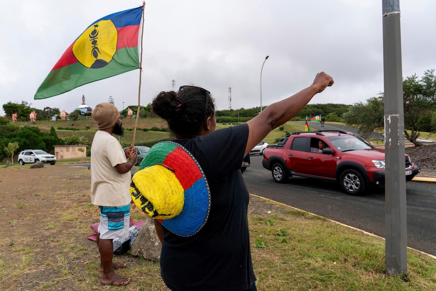 A man and woman waive Kanak flags at passing cars