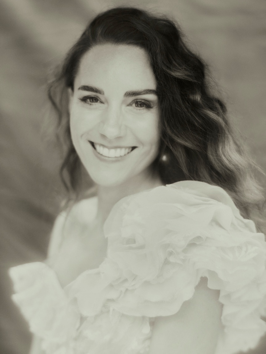 Kate Middleton smiles at the camera in this black and white portrait photo of her in a white dress.