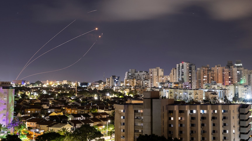 Rocket trails are seen in the night sky over a city skyline