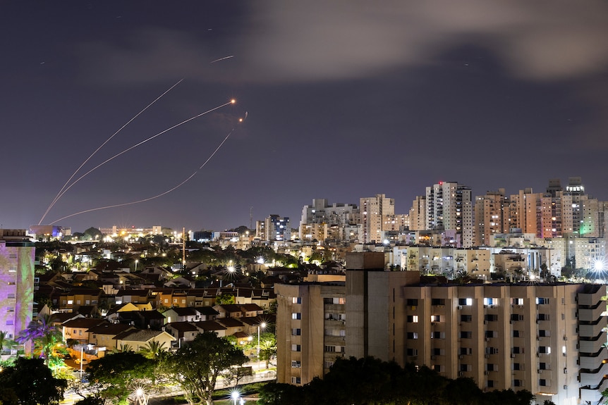 Rocket trails are seen in the night sky over a city skyline