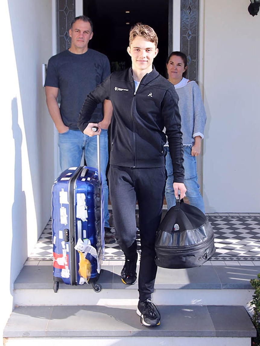 A young man wheels a suitcase while his parents watch on.