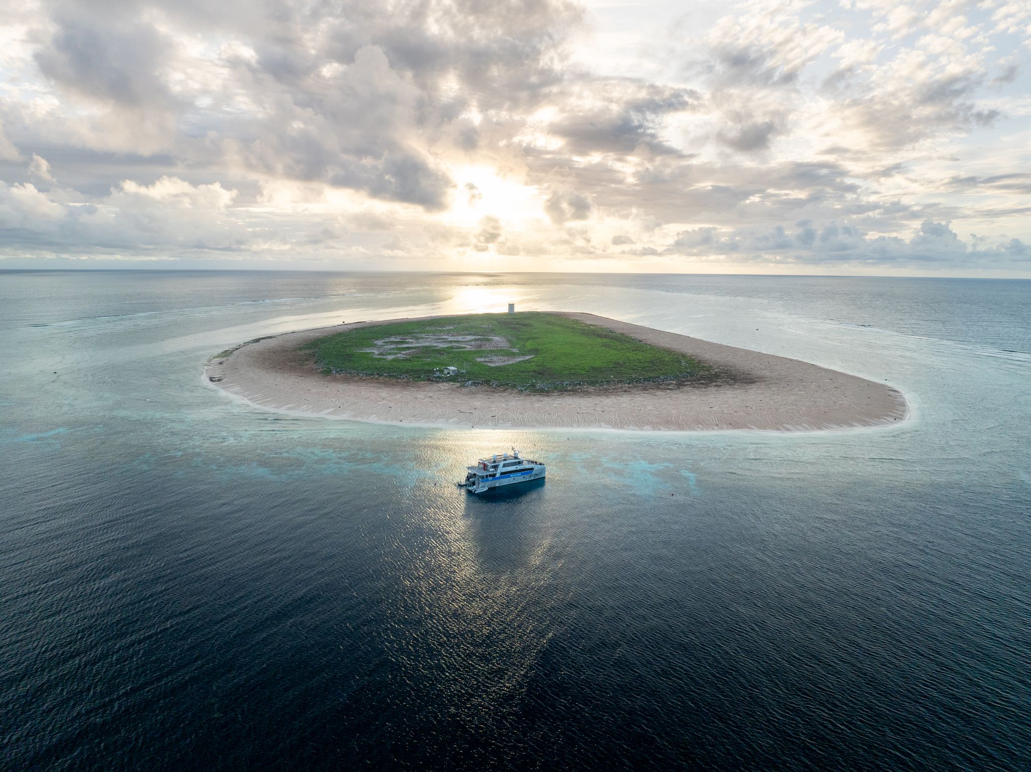 A boat next to a small sandy island with a bit of grass in the middle.