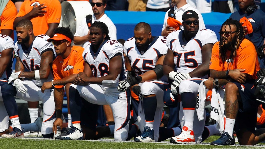 Six footballers kneel on the sideline during a pre-game national anthem.