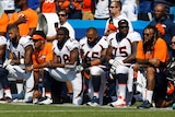 Six footballers kneel on the sideline during a pre-game national anthem.