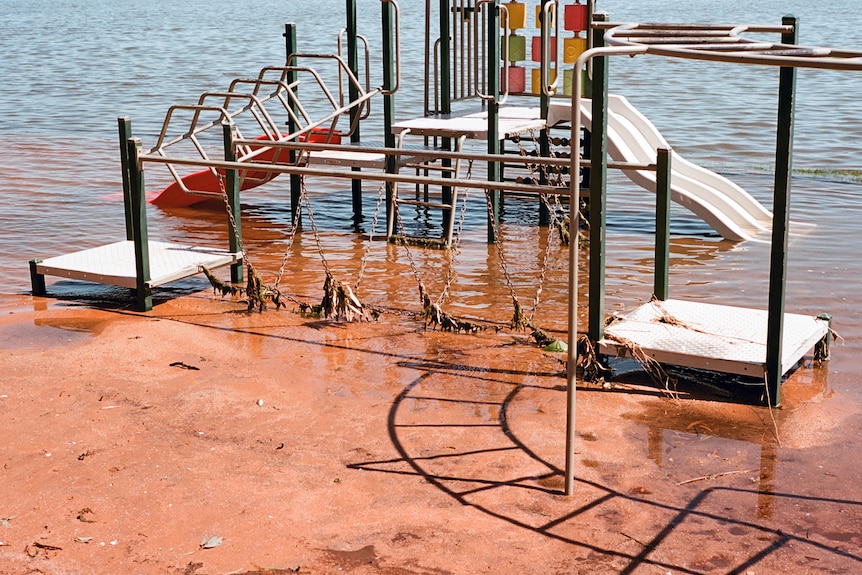 A playground surrounded by water, partly submerged, red mud, blue waters.