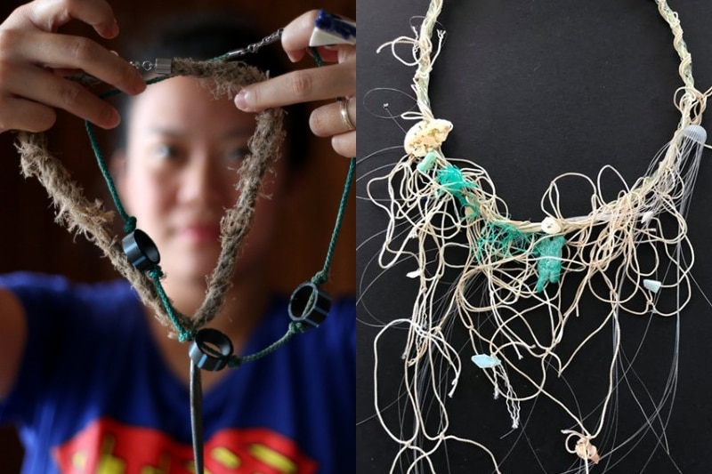 A woman holds a necklace made of rope, sinkers and plastic piping, and a necklace made of string and fishing line on a table.