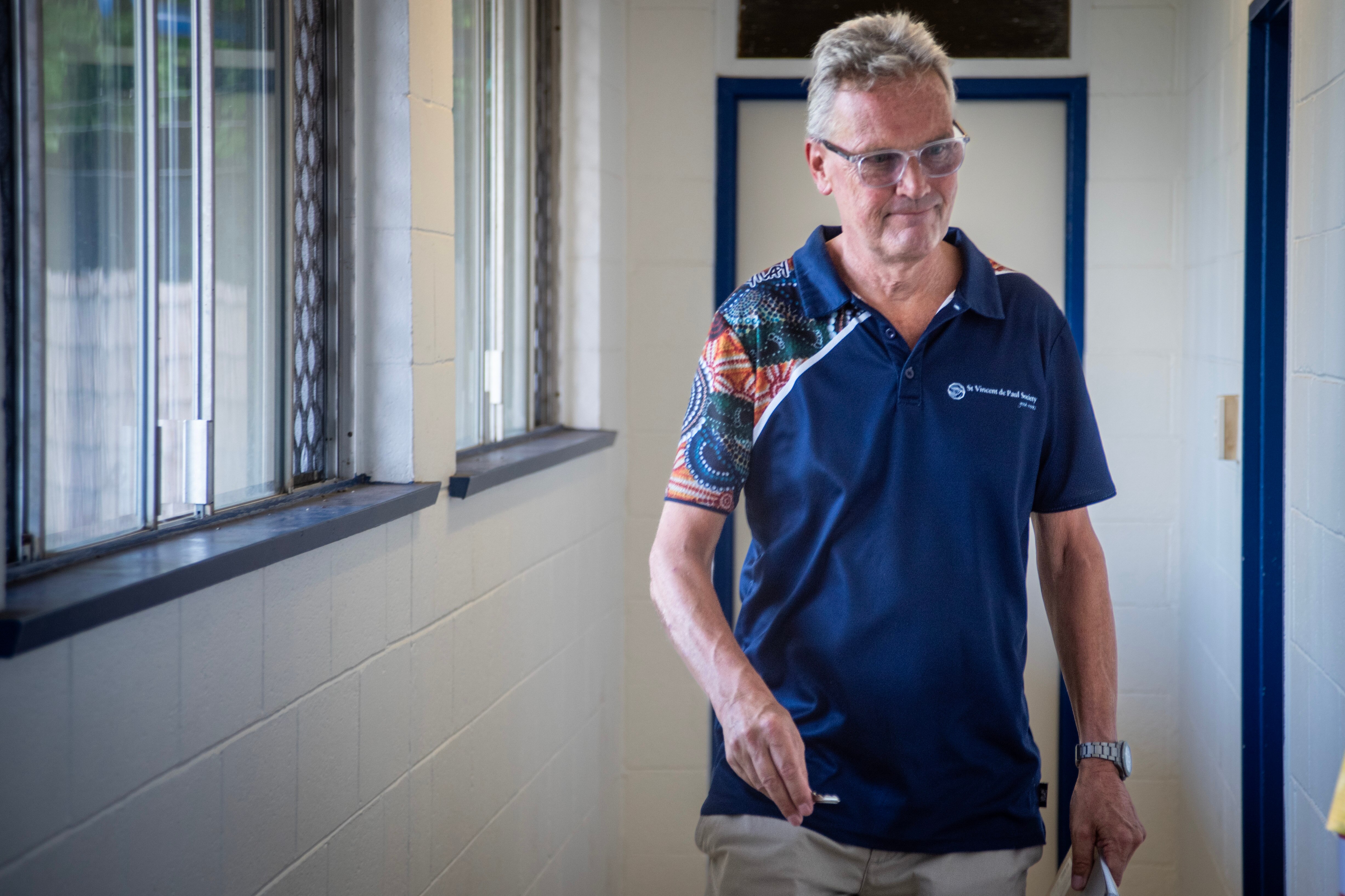 An older man walks in a walkway with a key smiling. 