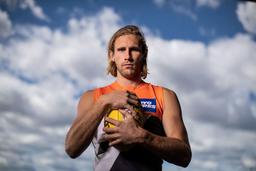 A footballer with long blond hair holds a ball