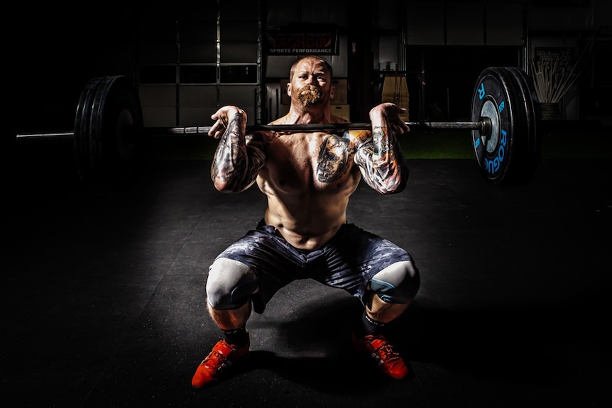 A bearded man strains to lift a barbell weight.