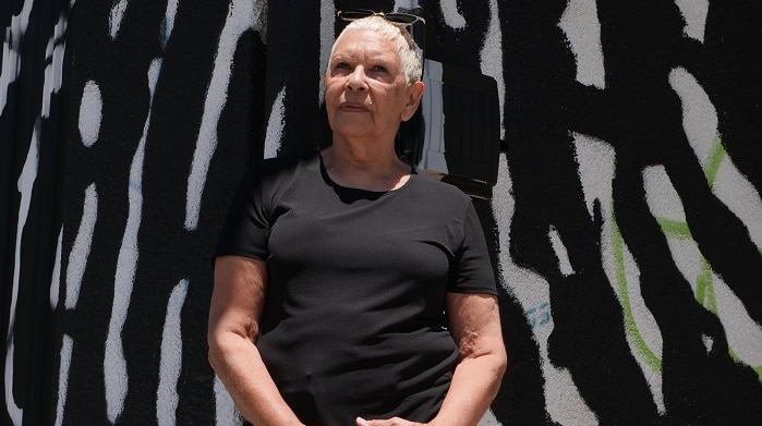 Indigenous woman and artist Glennys Briggs stands in front of two-storey building on a sunny day.