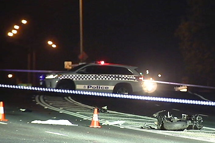 The wreckage of a motorcycle crash the foreground surrounded by police tape and a police car in the background.