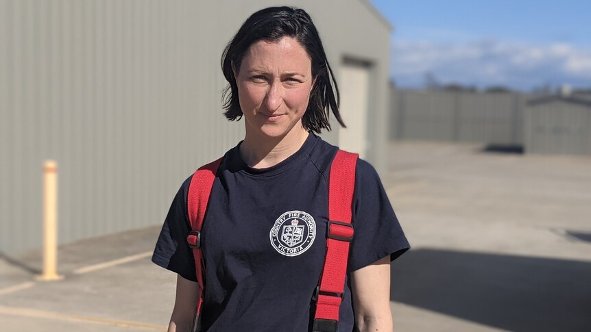 A young woman wearing firefighting overalls looks straight down the camera with a serious look on her face