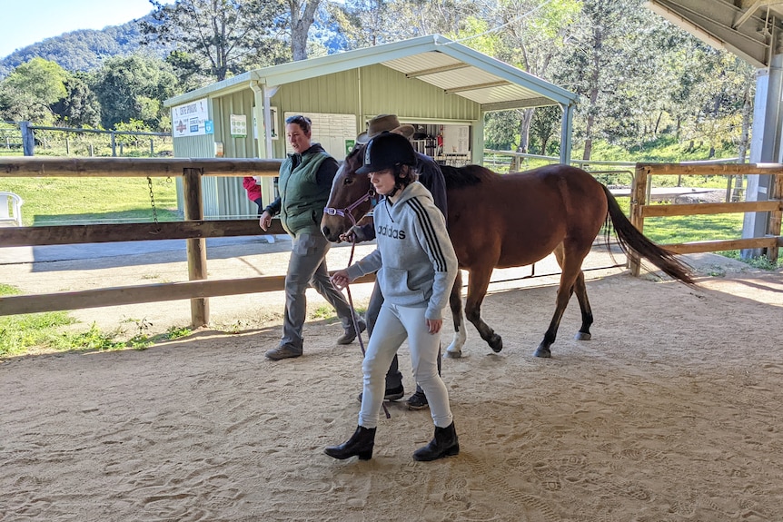 Two people walk around an arena with a horse