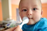 Baby in blue shirt being fed with spoon