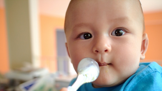 Baby in blue shirt being fed with spoon