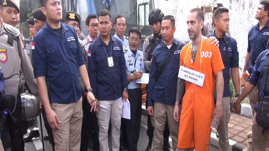 Orange jumpsuit-clad prisoner Dimitar Nikolove stands in the middle of a group of police and jail officials.