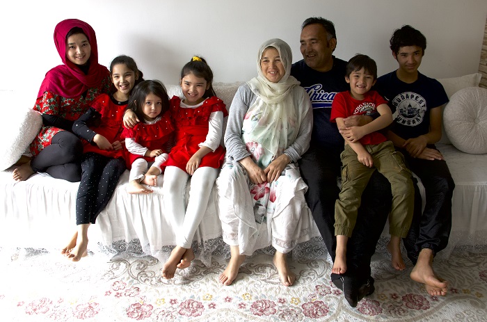 An Afghan family sits on a couch smiling at the camera