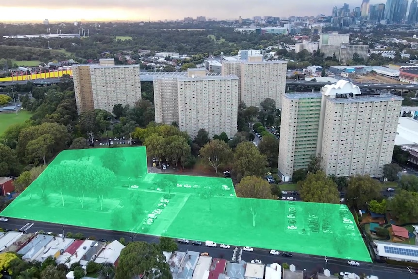 An aerial view of public housing towers and a green highlighted zone of vacant land beside them where a build is planned.