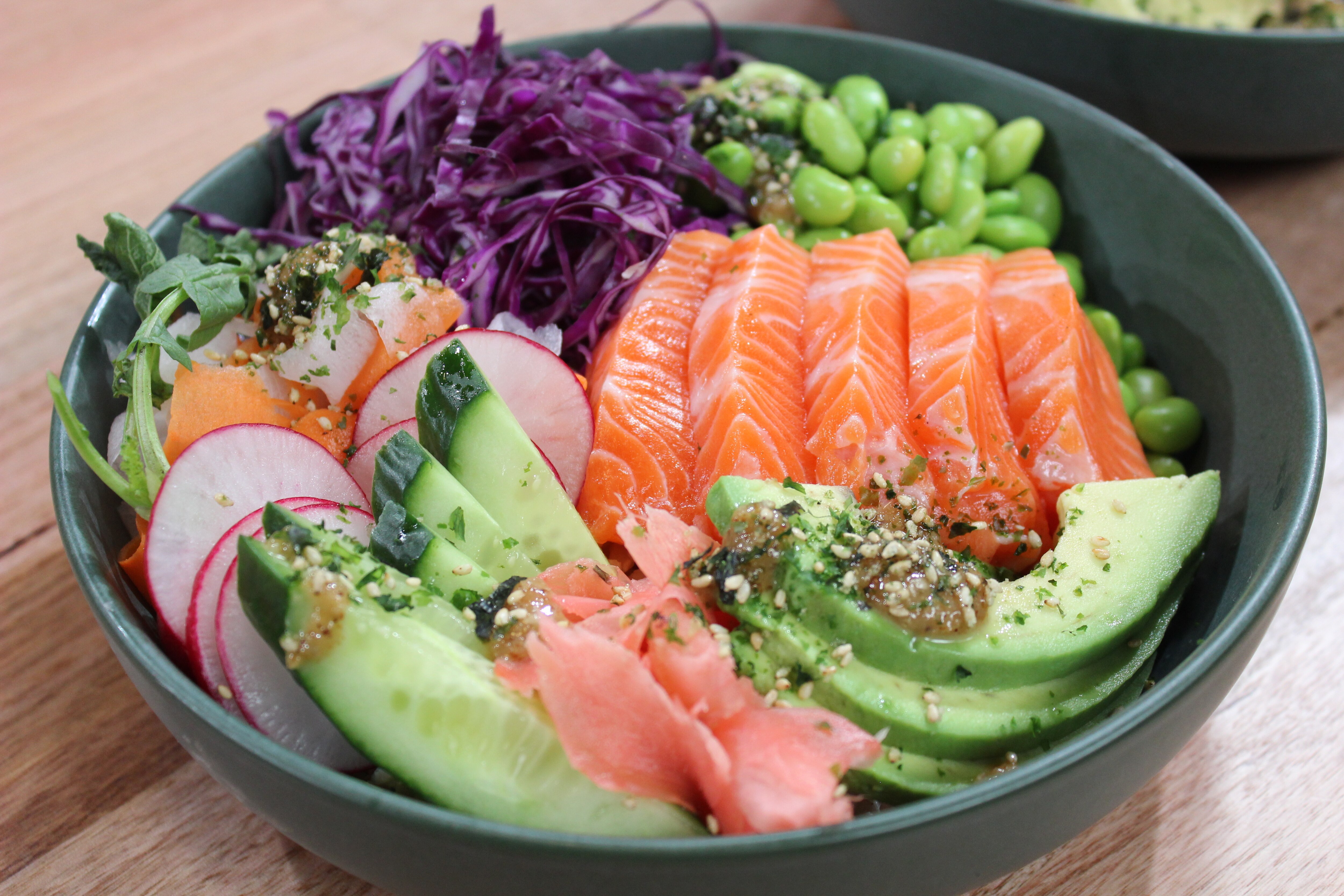 A picture   of a finished dish of a salmon poke bowl in a serving bowl on bench top finished with seeds and herbs