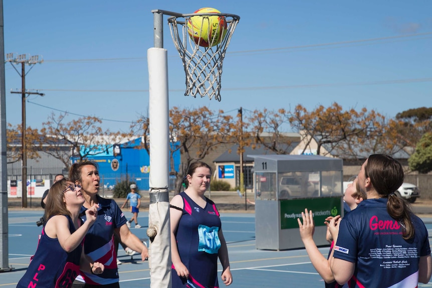 Three netball players watch as a ball enters the net