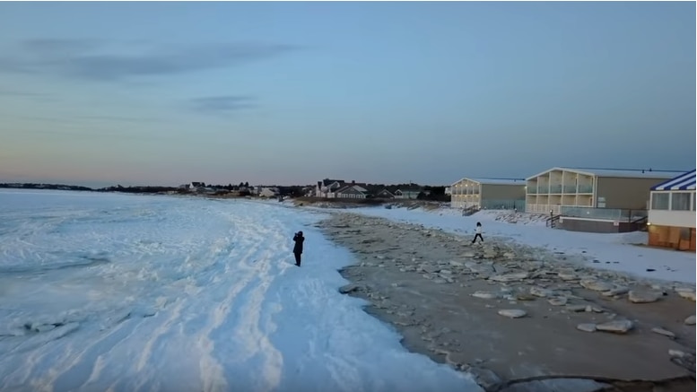 A person stands on the frozen ocean, just next to a beach at twilight