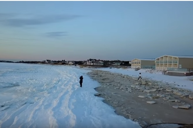 A person stands on the frozen ocean, just next to a beach at twilight