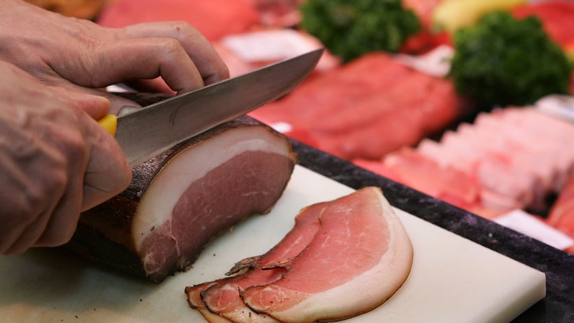 Meat butchery display with hand cutting bacon