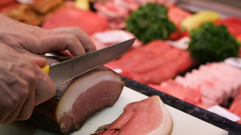 Meat butchery display with hand cutting bacon.